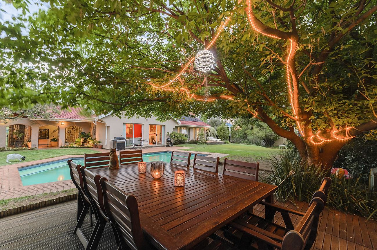 Beautiful tree with fairy lights and table adjacent pool early evening.